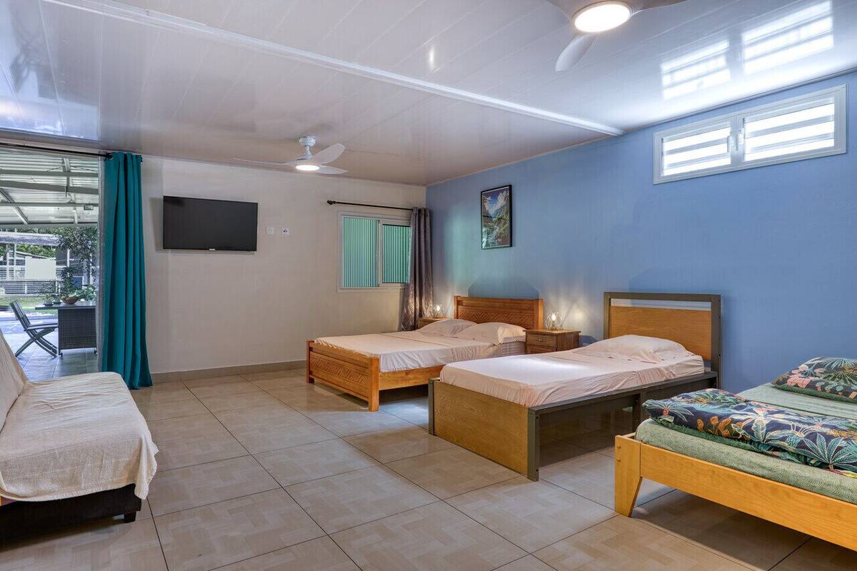 A room with two wooden beds, a sofa, a TV, and a ceiling fan.