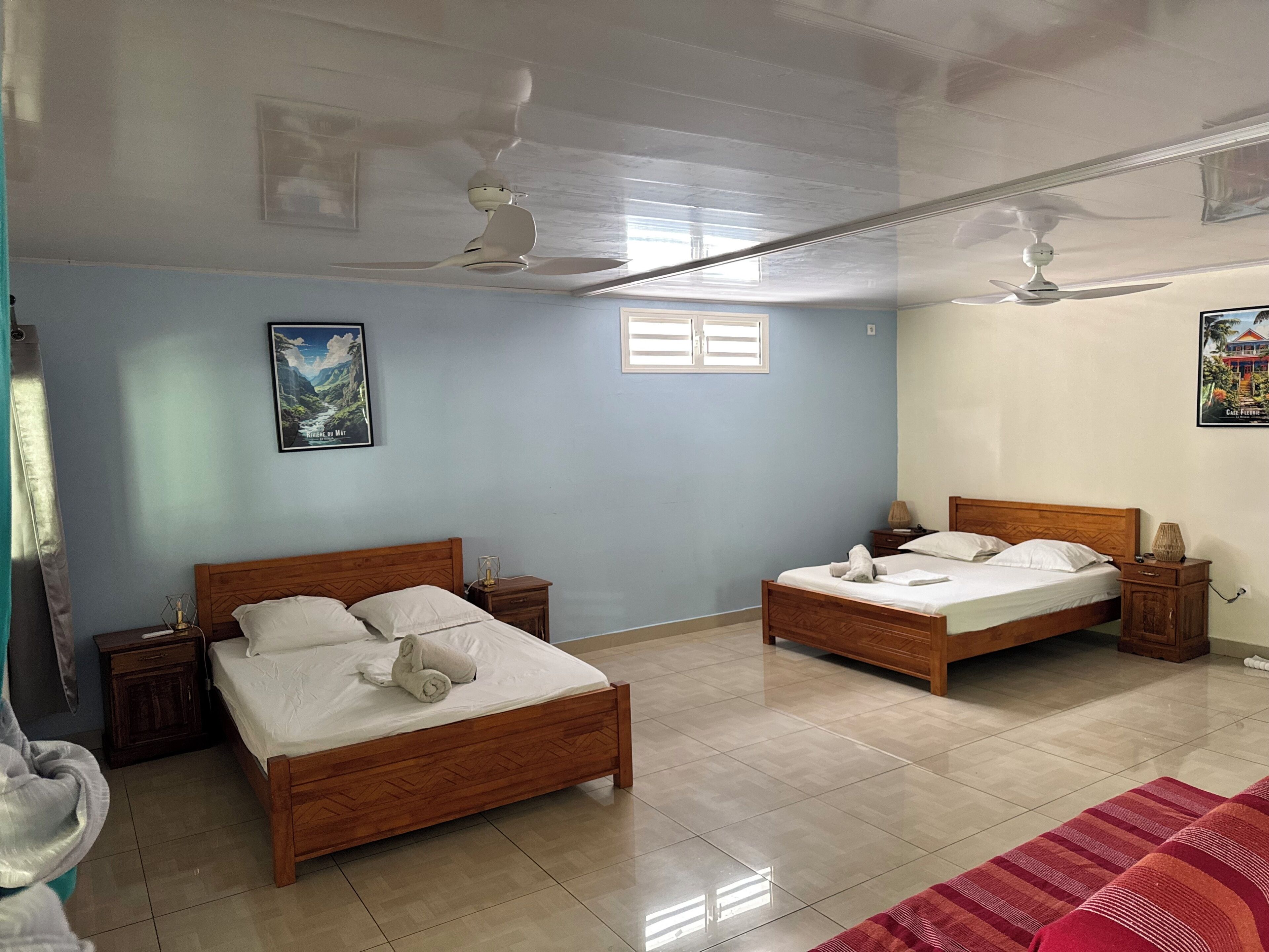 A room with two wooden beds, a ceiling fan, a window, and a framed picture on the wall.