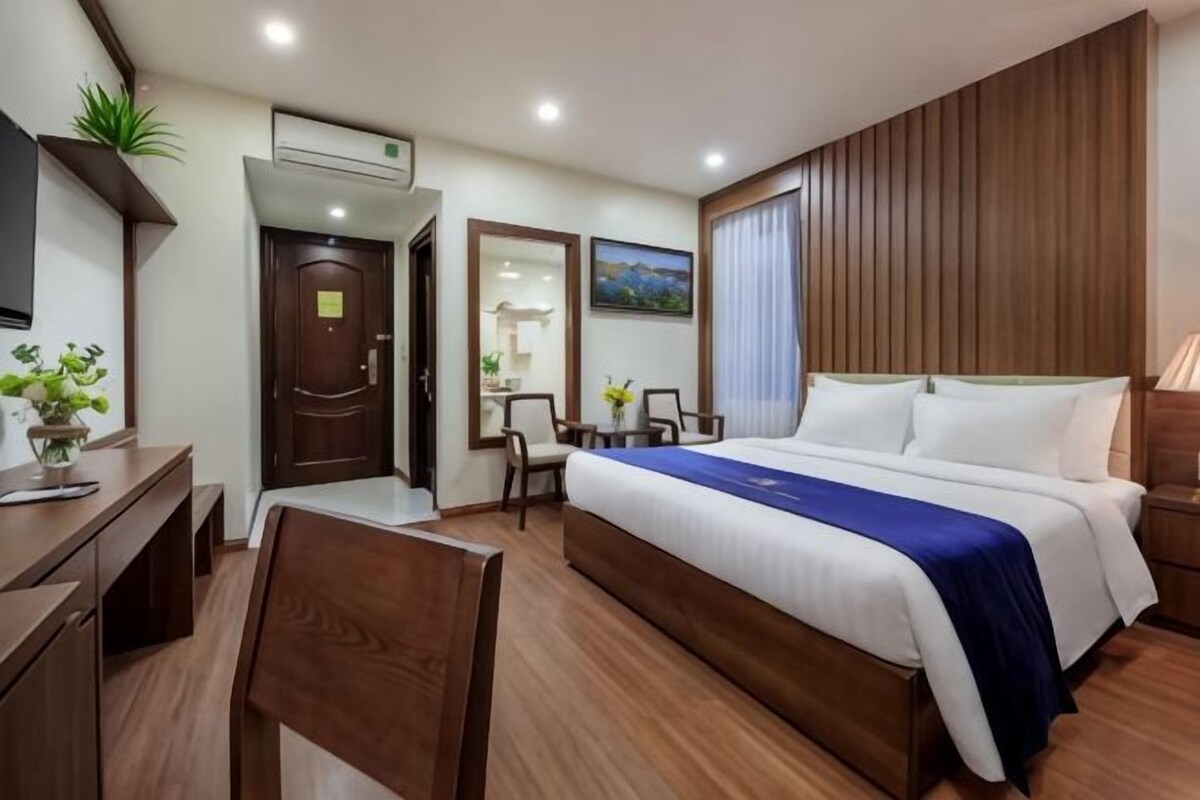 A hotel room with a bed, a desk, a chair, a mirror, and a window.