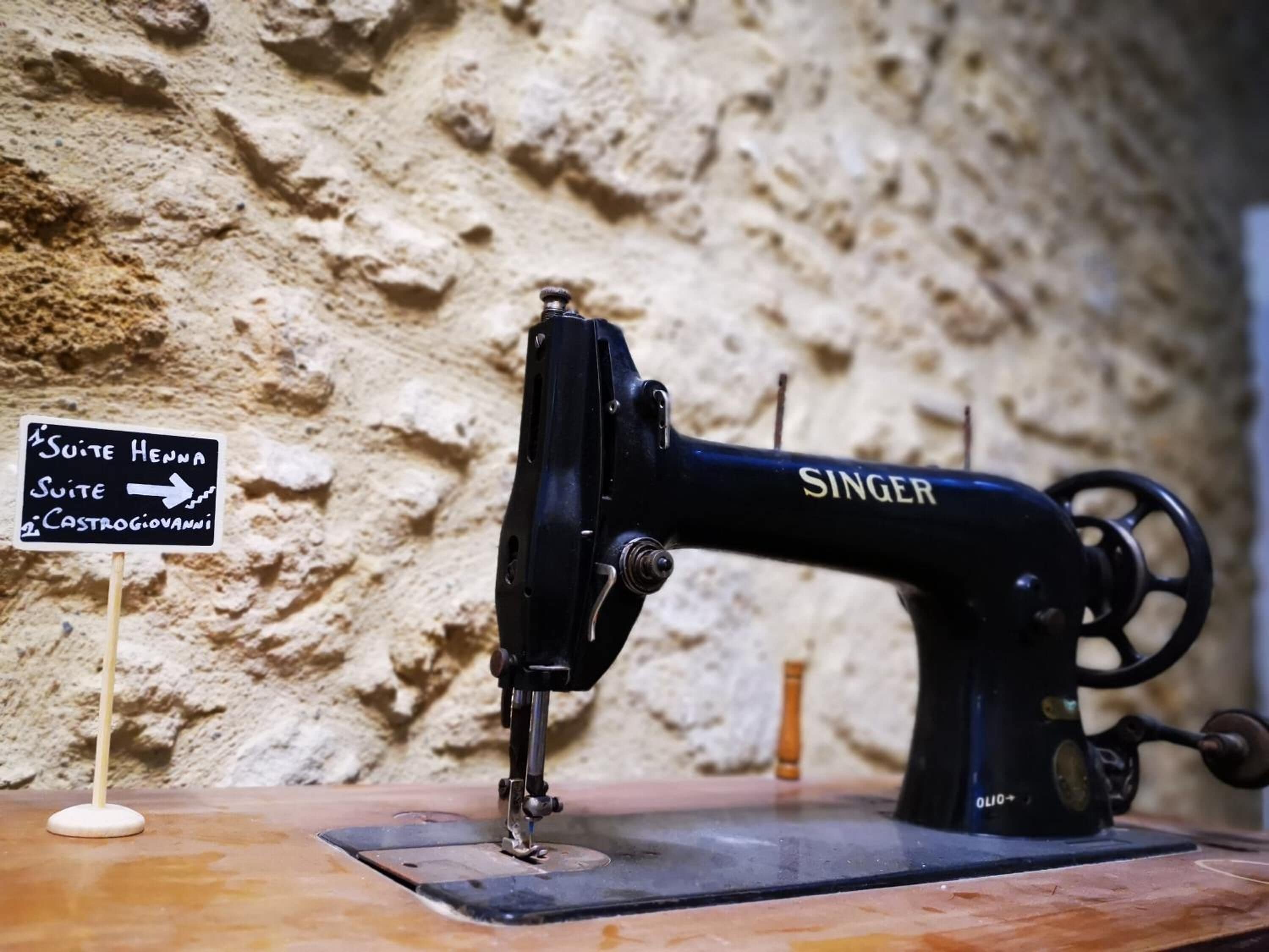 A Singer sewing machine on a wooden table against a textured wall.