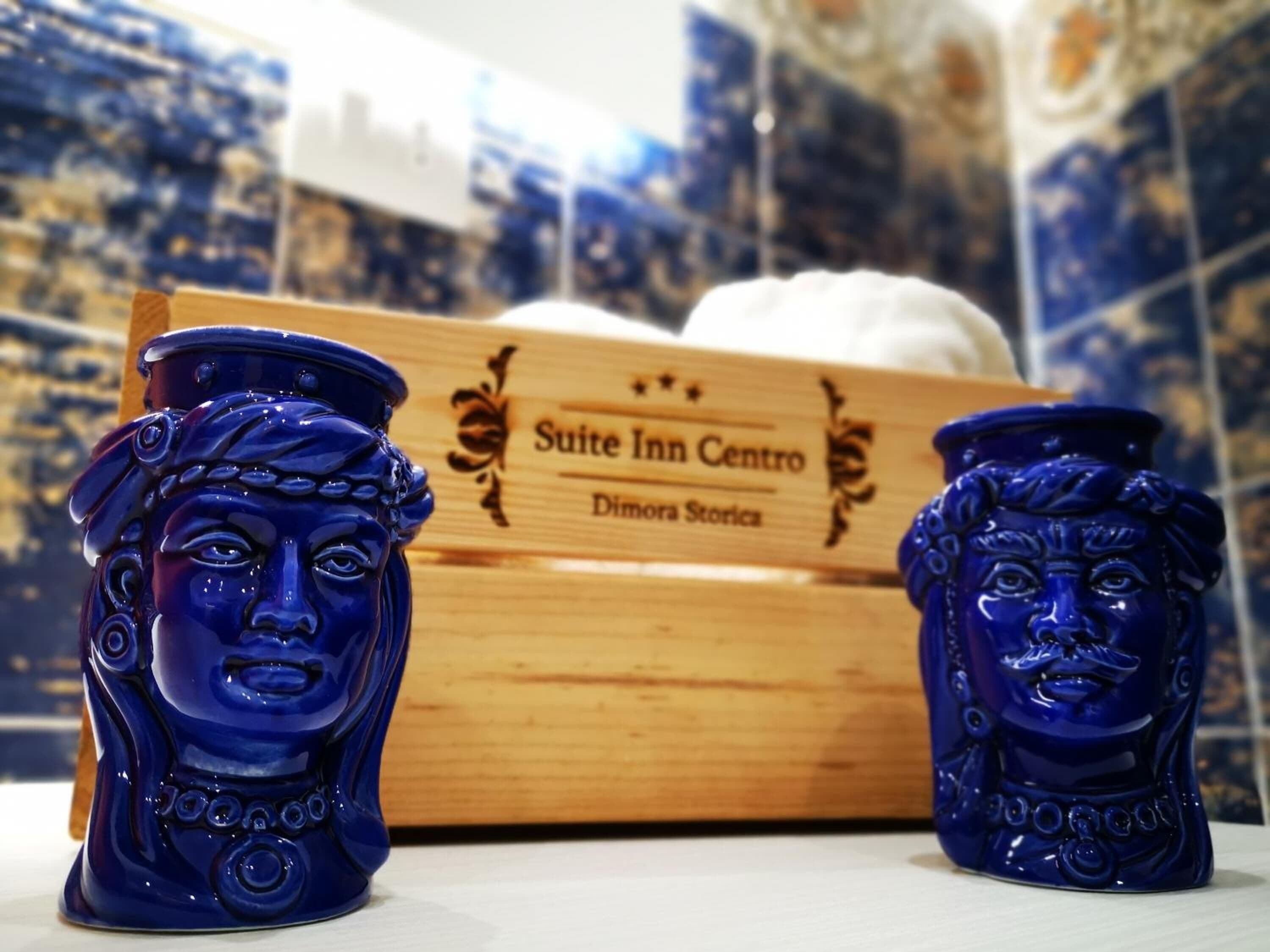Dos jarrones azules de cerámica con diseños intrincados, situados frente a una caja de madera con la etiqueta "Suite Inn Centro Dimora Stories".