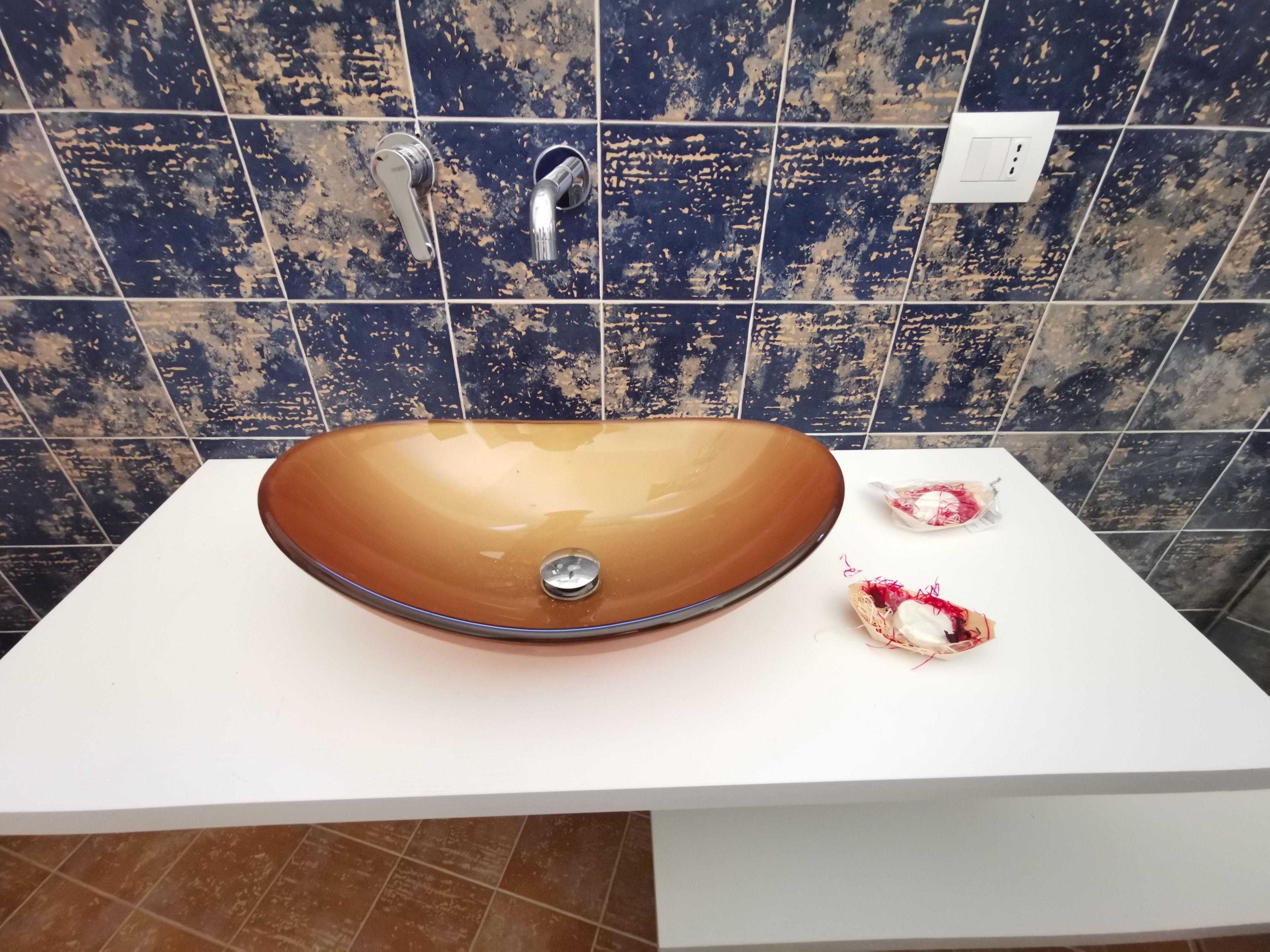 A bathroom with a large, oval-shaped vessel sink on a white countertop, a faucet, and a wall with blue tiles.