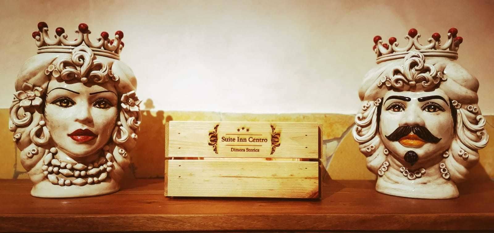 Two ceramic figurines with crowns on a shelf, a wooden box labeled "Suite Inn Centro," and a partial view of a wall.