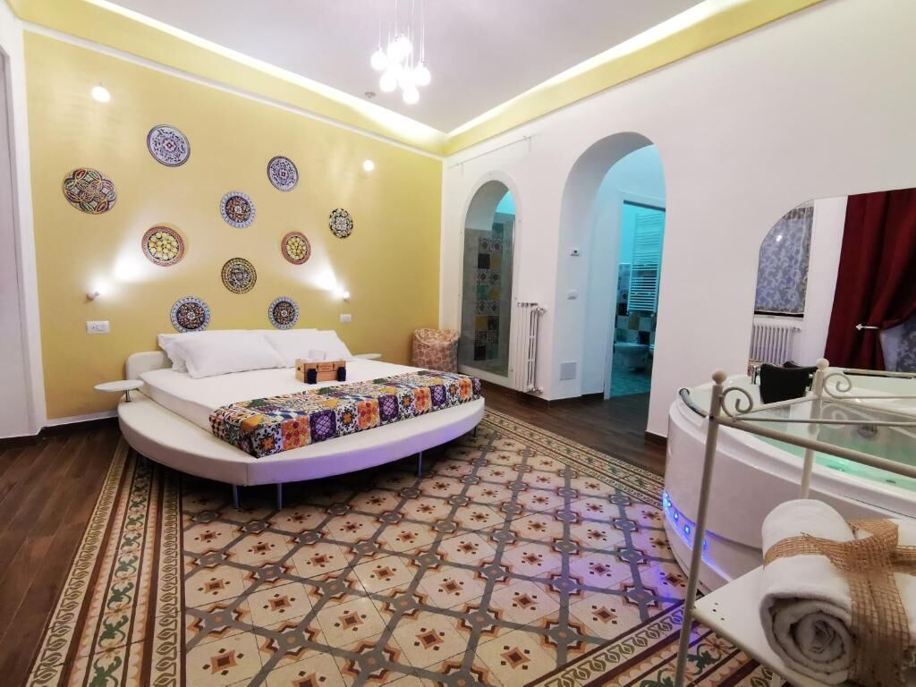 A modern bedroom with a curved bed, decorative wall plates, a patterned rug, and a glass table with towels.