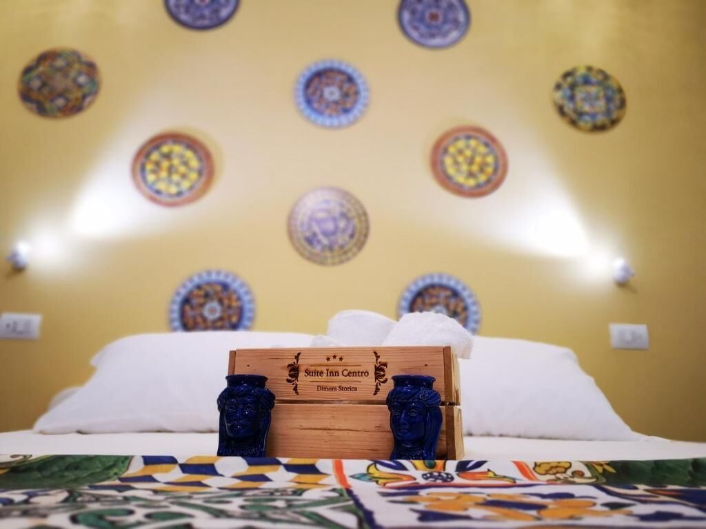 Un lit avec une tête de lit en bois, une boîte décorative portant l’inscription « Suite Inn Centro » et une couvre-lit à motifs.