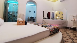 Une chambre d’hôtel comprenant un lit, une coiffeuse avec un miroir, une petite table et un espace douche.