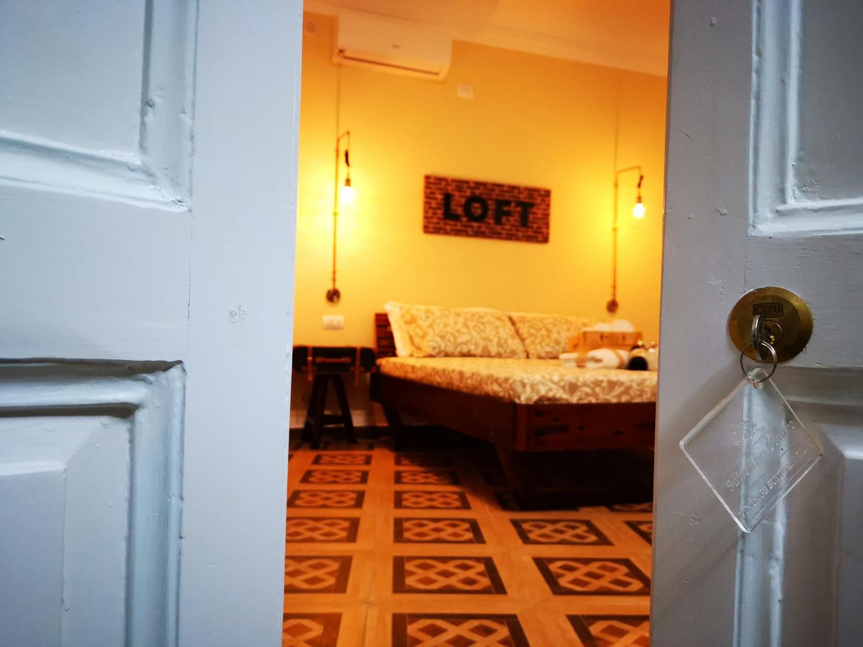 A room with a bed, a wall-mounted sign reading "LOFT", and a patterned floor.