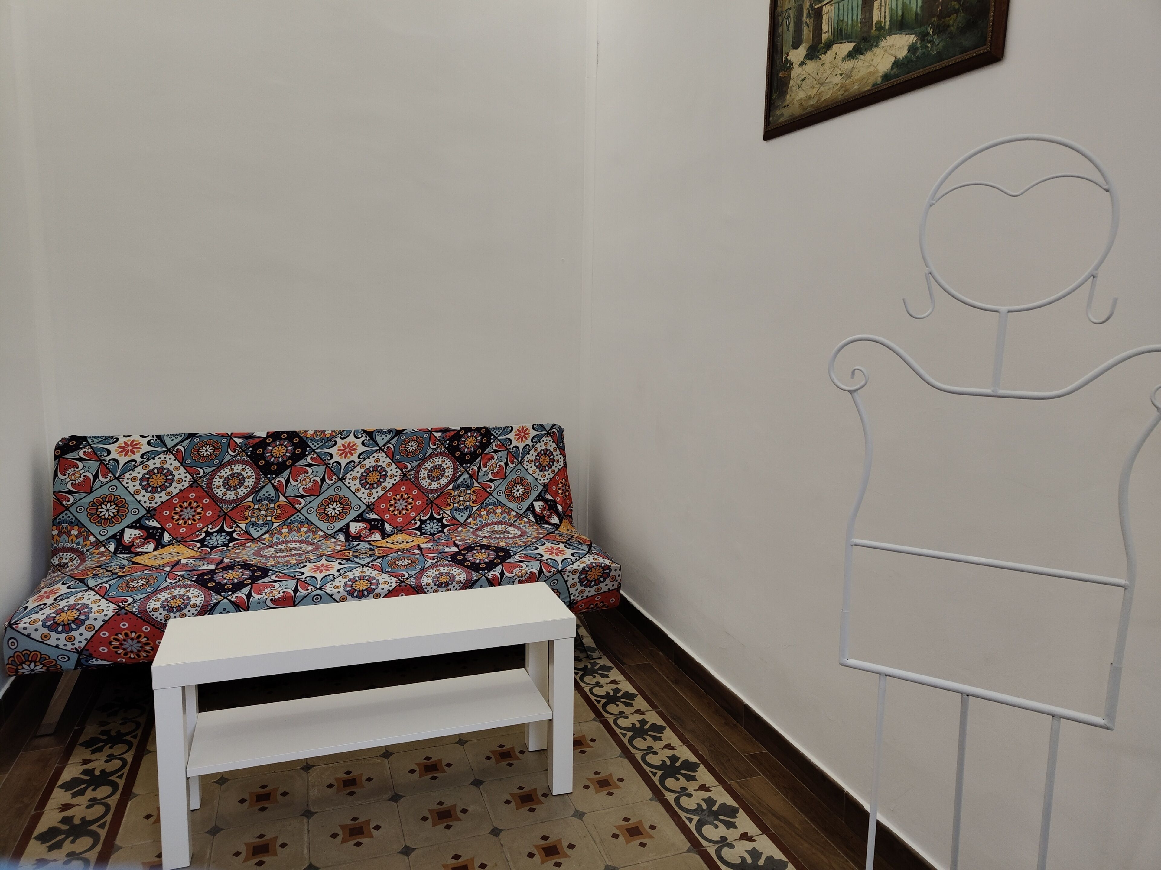 A room with a patterned sofa, a white bench, and a wall with a simple line drawing.