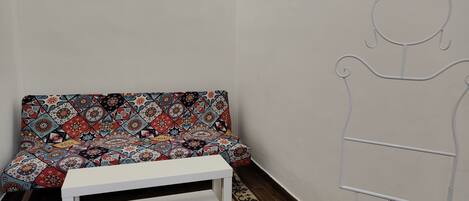 Una habitación con un sofá estampado, un banco blanco y una pared con un dibujo lineal sencillo.