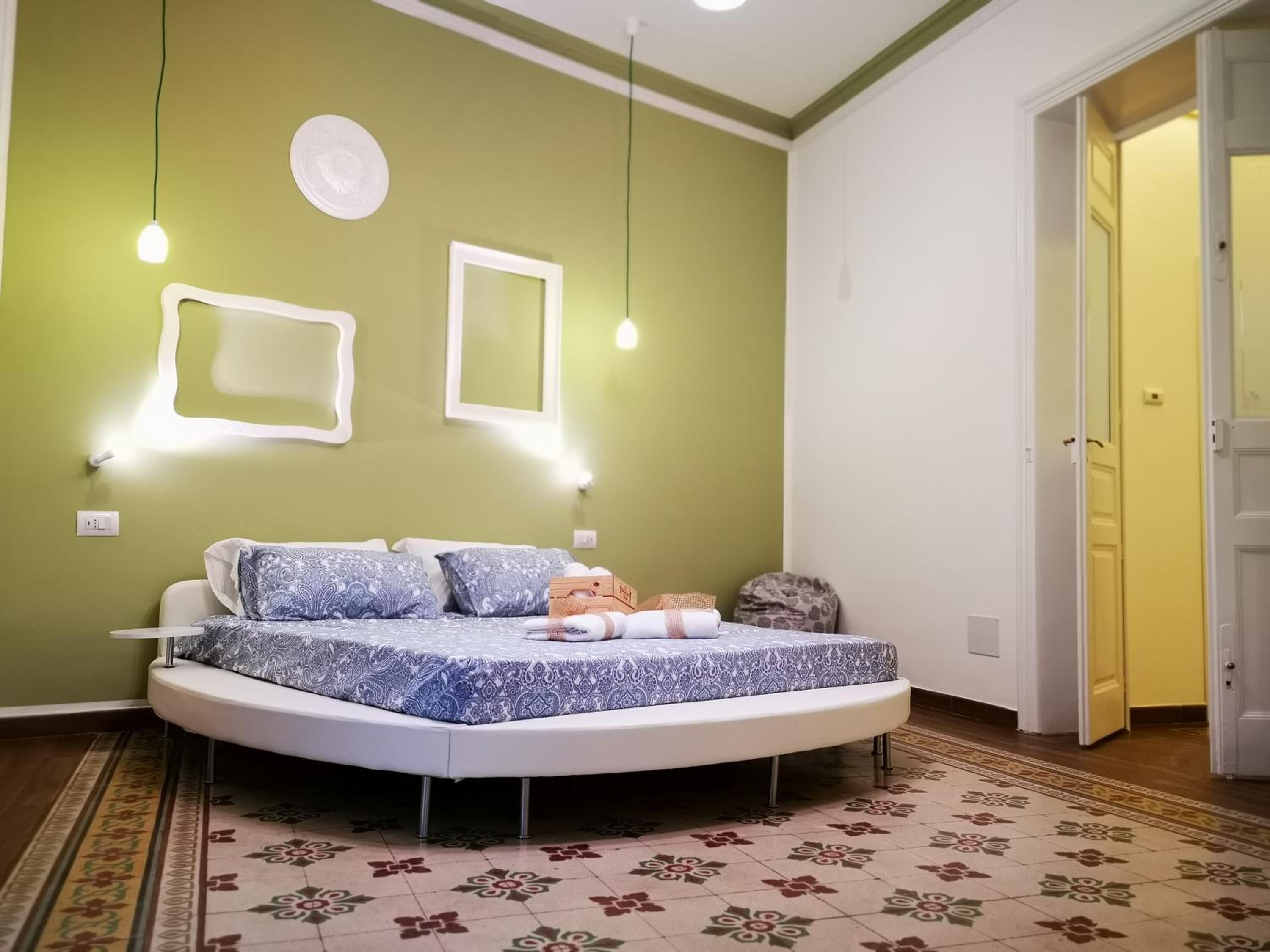 A round bed with a patterned bedspread, a bedside table, and a wall-mounted light fixture.