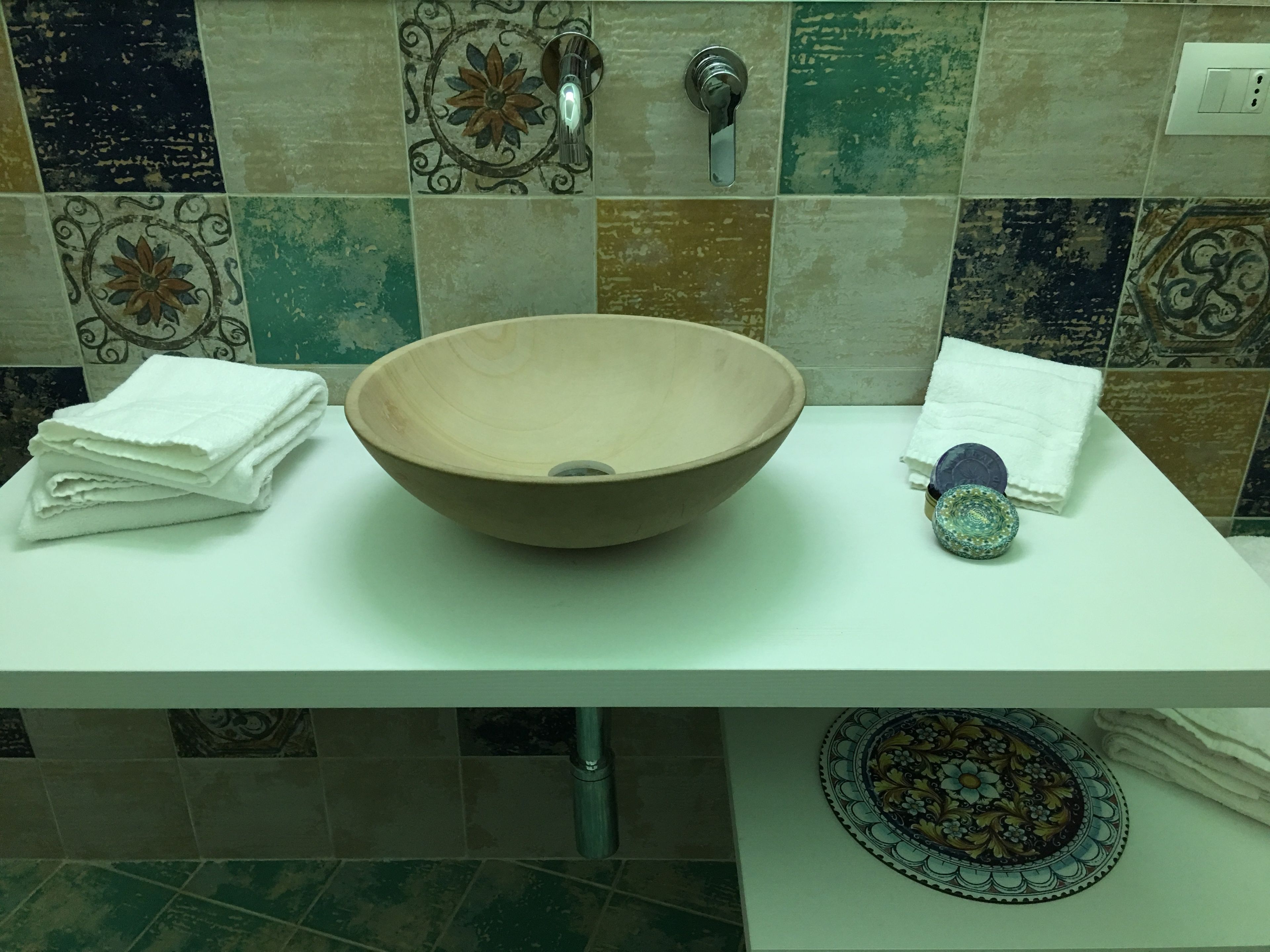 A bathroom with a large, round, beige sink, a white countertop, and a decorative tile backsplash.