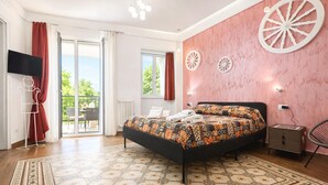 Une chambre à coucher avec un lit, une télévision, une chaise, une petite table et une fenêtre avec des rideaux.