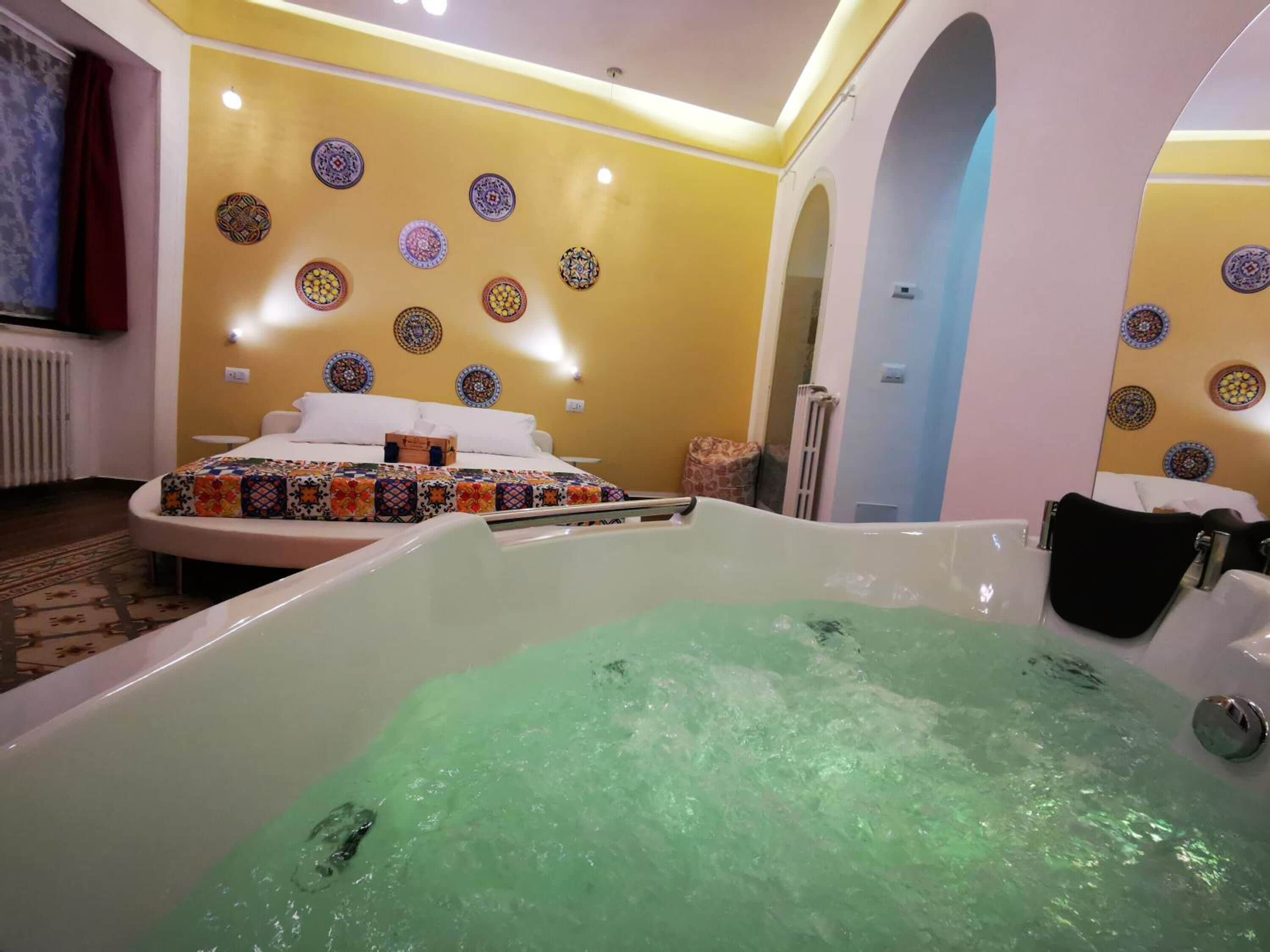 Habitació d'hotel amb una banyera gran plena d'aigua, un llit amb un estovat de colors i plats decoratius a la paret.