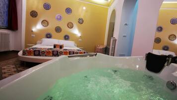 Habitació d'hotel amb una banyera gran plena d'aigua, un llit amb un estovat de colors i plats decoratius a la paret.