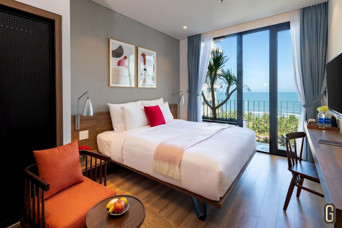 Een moderne hotelkamer met een groot bed, een bureau en uitzicht op zee.