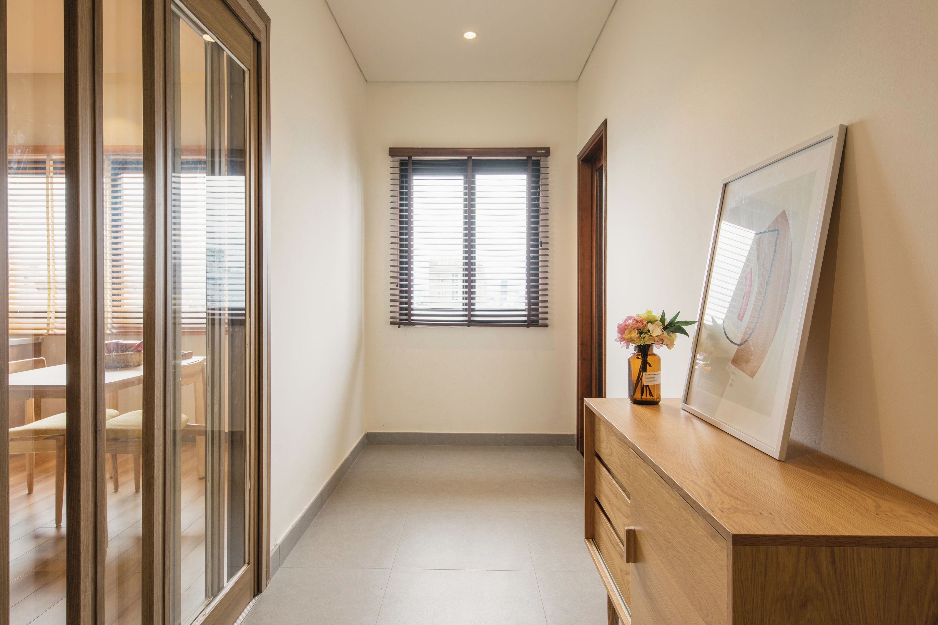 A hallway with a wooden cabinet, a framed picture, and a window with blinds.