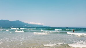A beach with waves, a distant mountain, and a clear sky. - The Glomad Boutique Danang by DS (Da Nang)