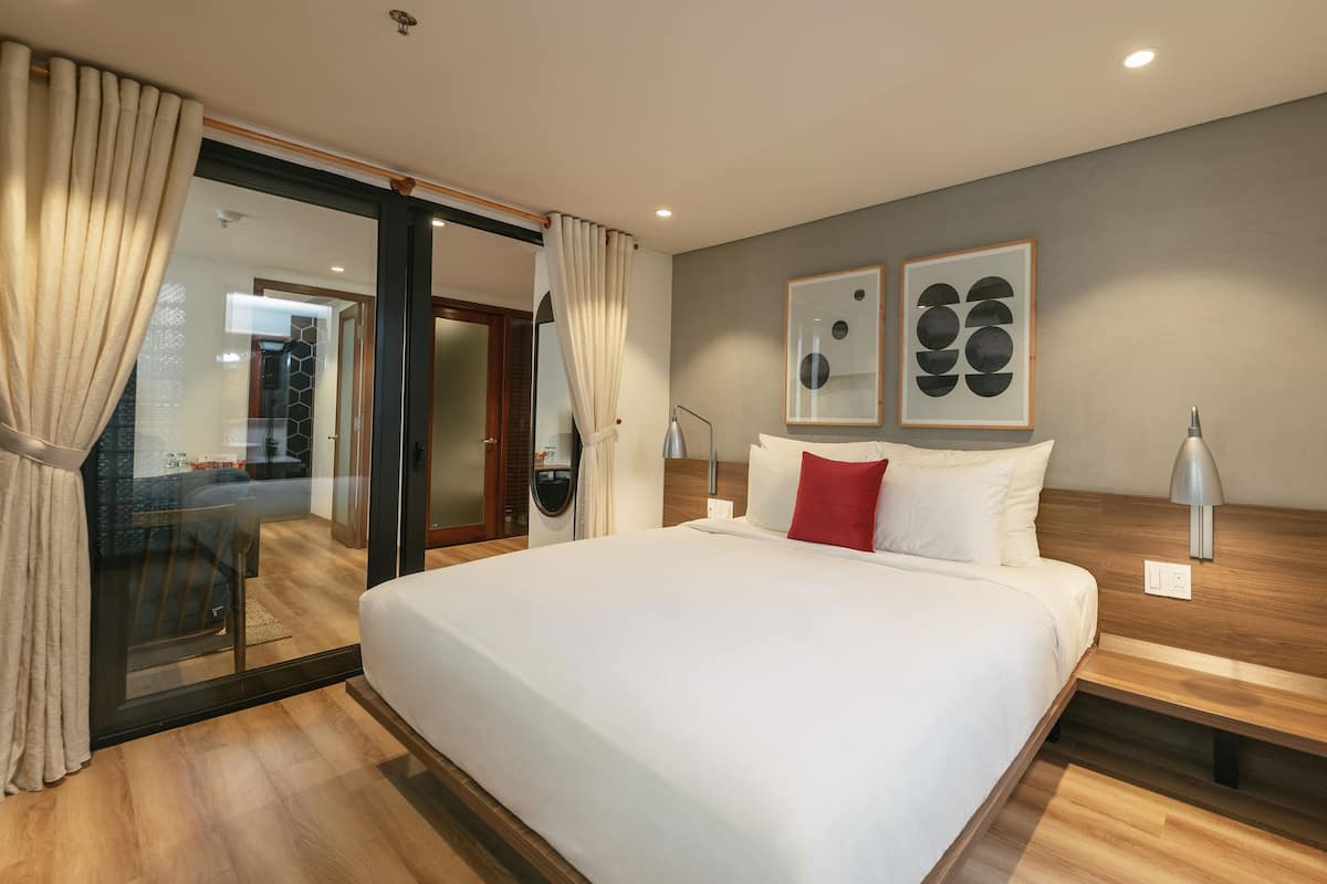 Een moderne hotelkamer met een groot bed, een houten hoofdbord, een glazen deur naar een balkon, en twee ingelijste abstracte schilderijen aan de muur.