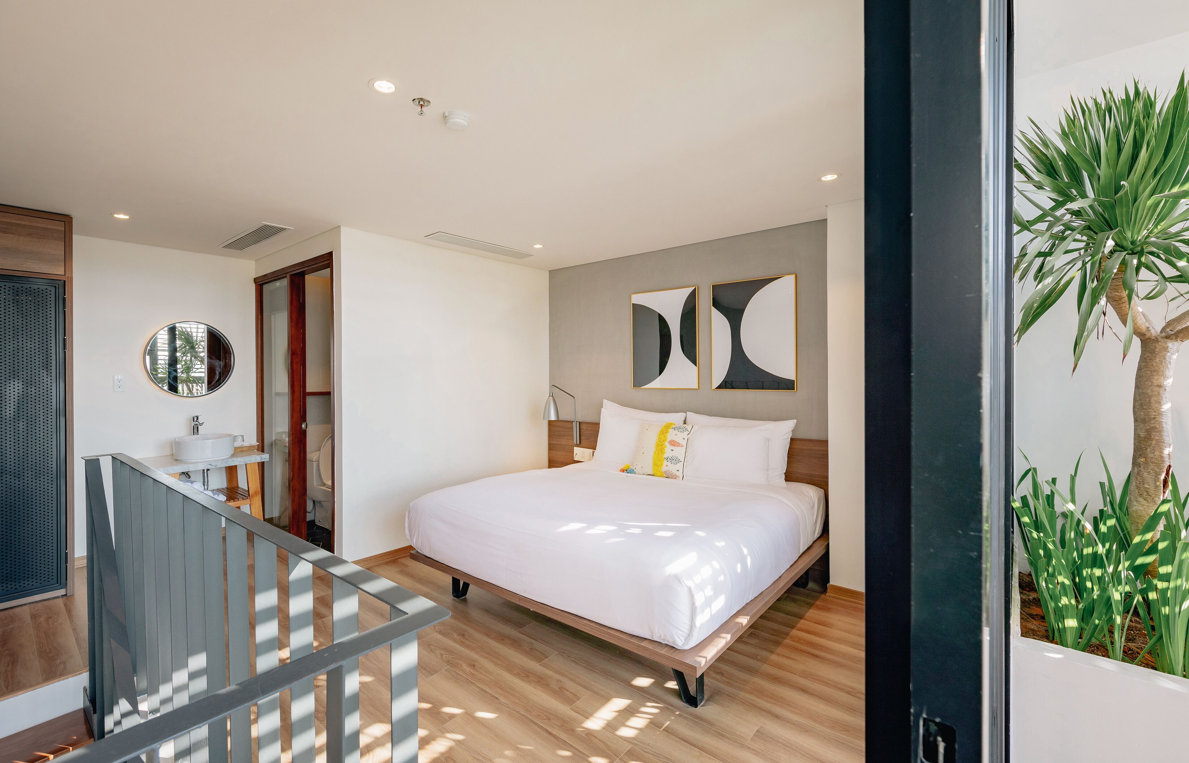Un dormitorio moderno con una cama grande, suelo de madera, un espejo redondo, un baño con lavamanos y una escalera.