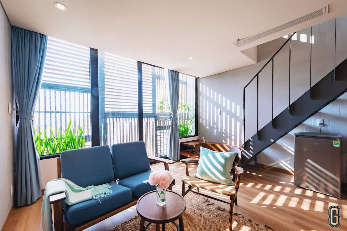 Een moderne woonkamer met een bank, stoelen, een salontafel en een bijzettafeltje met bloemen. Er is een trap met een leuning en een koelkast.