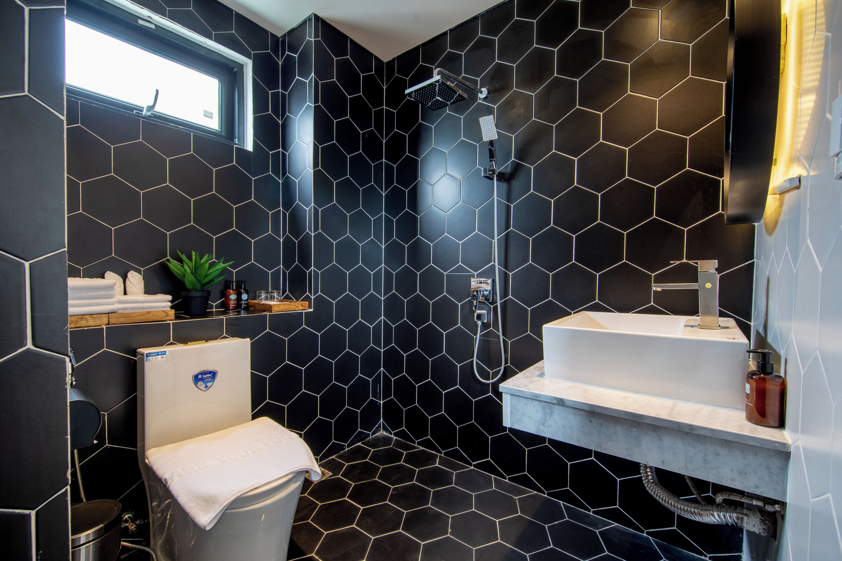 Un baño moderno con un patrón de azulejos hexagonales negros, un lavabo blanco y una ducha con cabezal de ducha de mano.