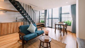 A modern living room with a blue sofa, a wooden coffee table, a dining area with a table and chairs, a kitchen area with a microwave, and a staircase. - The Glomad Boutique Danang by DS (Da Nang)