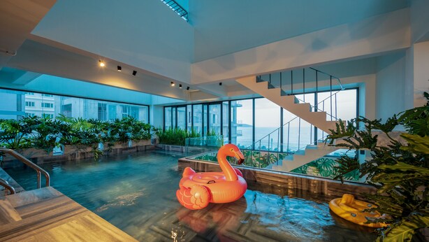 A spacious indoor pool area with a wooden deck, a glass staircase, and potted plants. - The Glomad Boutique Danang by DS (Da Nang)
