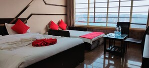 Habitación de hotel con una cama grande, dos camas más pequeñas, un escritorio con silla y vistas a las montañas a través de amplias ventanas.