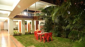 A covered outdoor dining area with a table and chairs, surrounded by lush greenery and a brick wall. - River Palace (Wai)