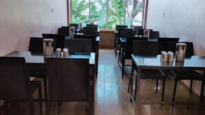 A restaurant with black chairs and tables, arranged in rows, with a view of greenery outside. - River Palace (Wai)