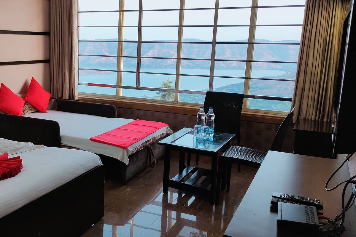 A hotel room with two beds, a desk, and a view of mountains and a lake.
