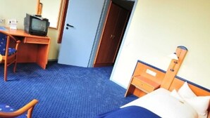 Una habitación de hotel con cama, escritorio y televisor, y una puerta.