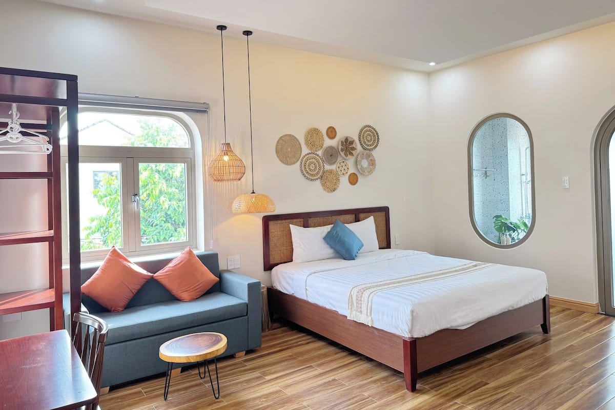 A bedroom with a bed, a sofa, a small table, and a hanging light fixture.