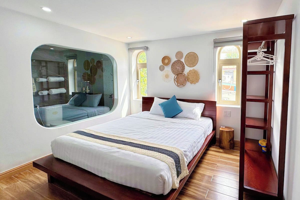 A bedroom with a large bed, a wooden floor, a window with a view, and a wooden wardrobe.
