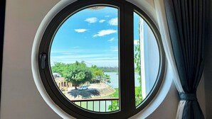 A round window with a view of a tree and a body of water. - Anriva Hoi An (Da Nang)