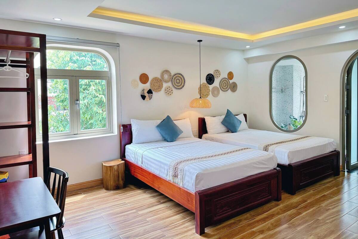 A bedroom with two beds, a wooden floor, a window, and wall decor.