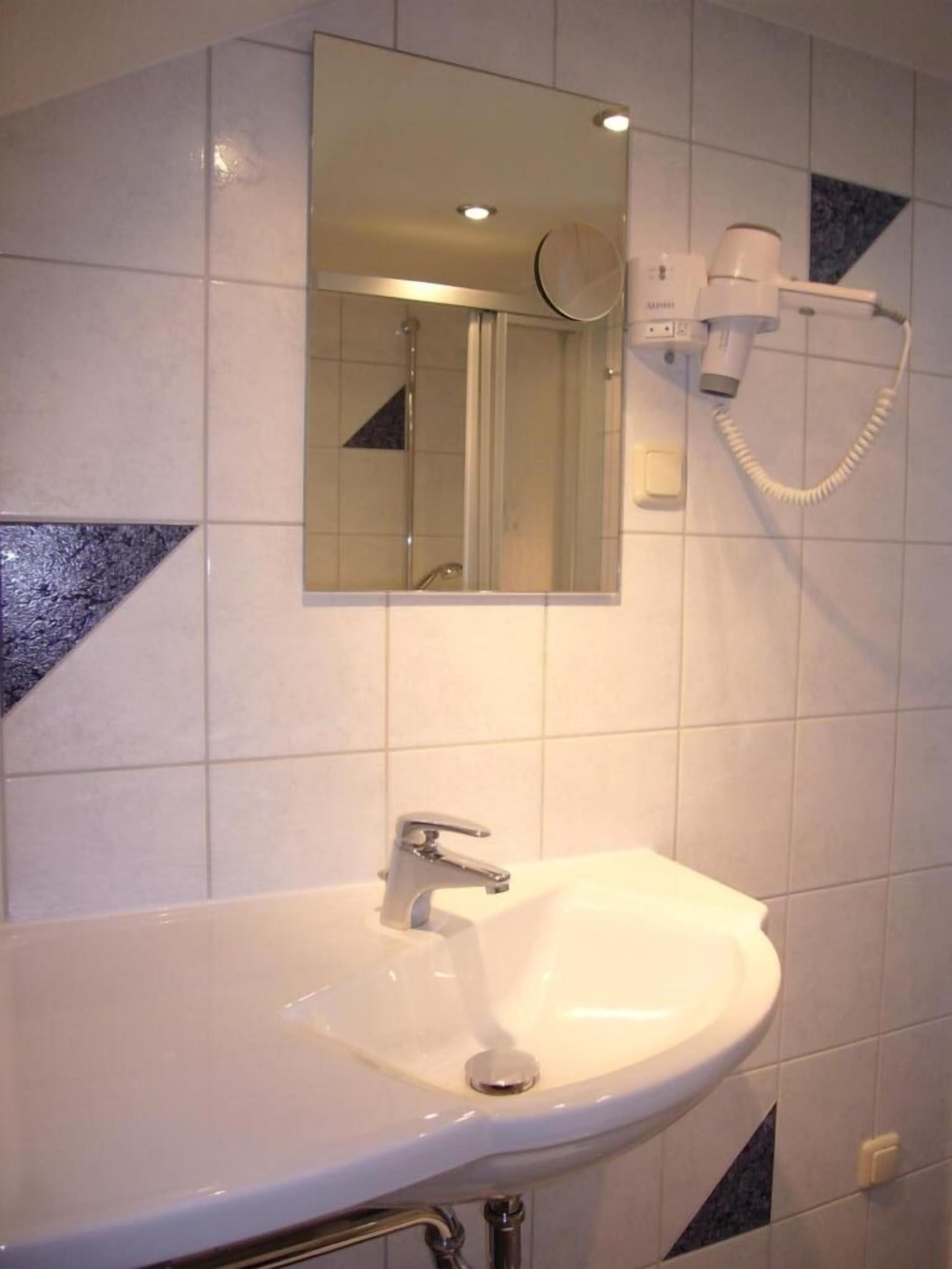 Een badkamer met een wit wastafel, een spiegel en een handdouche.