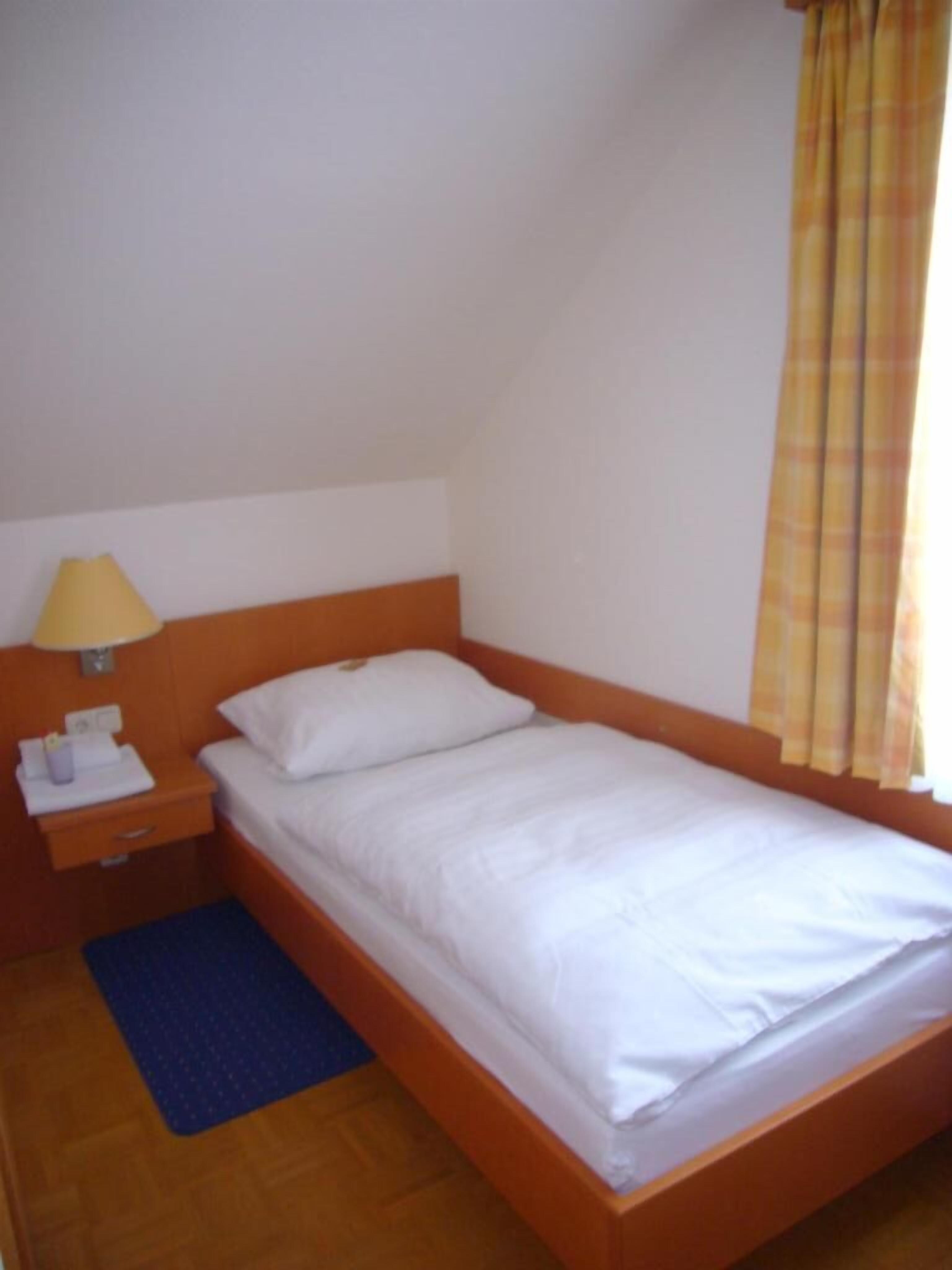 A single bed with white bedding in a room with a wooden headboard and a small bedside table with a lamp.