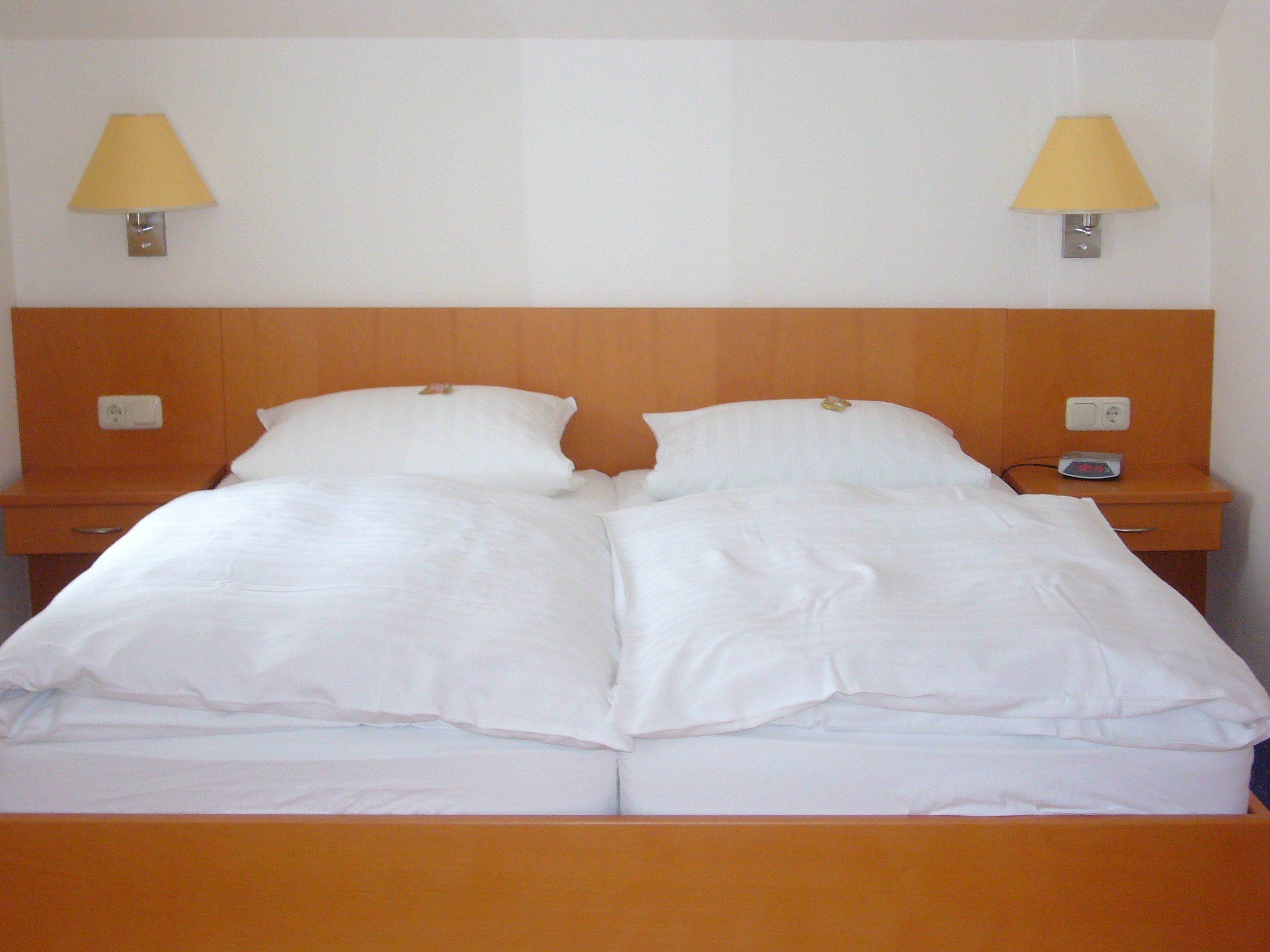 Un lit double avec du linge de lit blanc, deux tables de chevet avec des lampes et une tête de lit en bois.