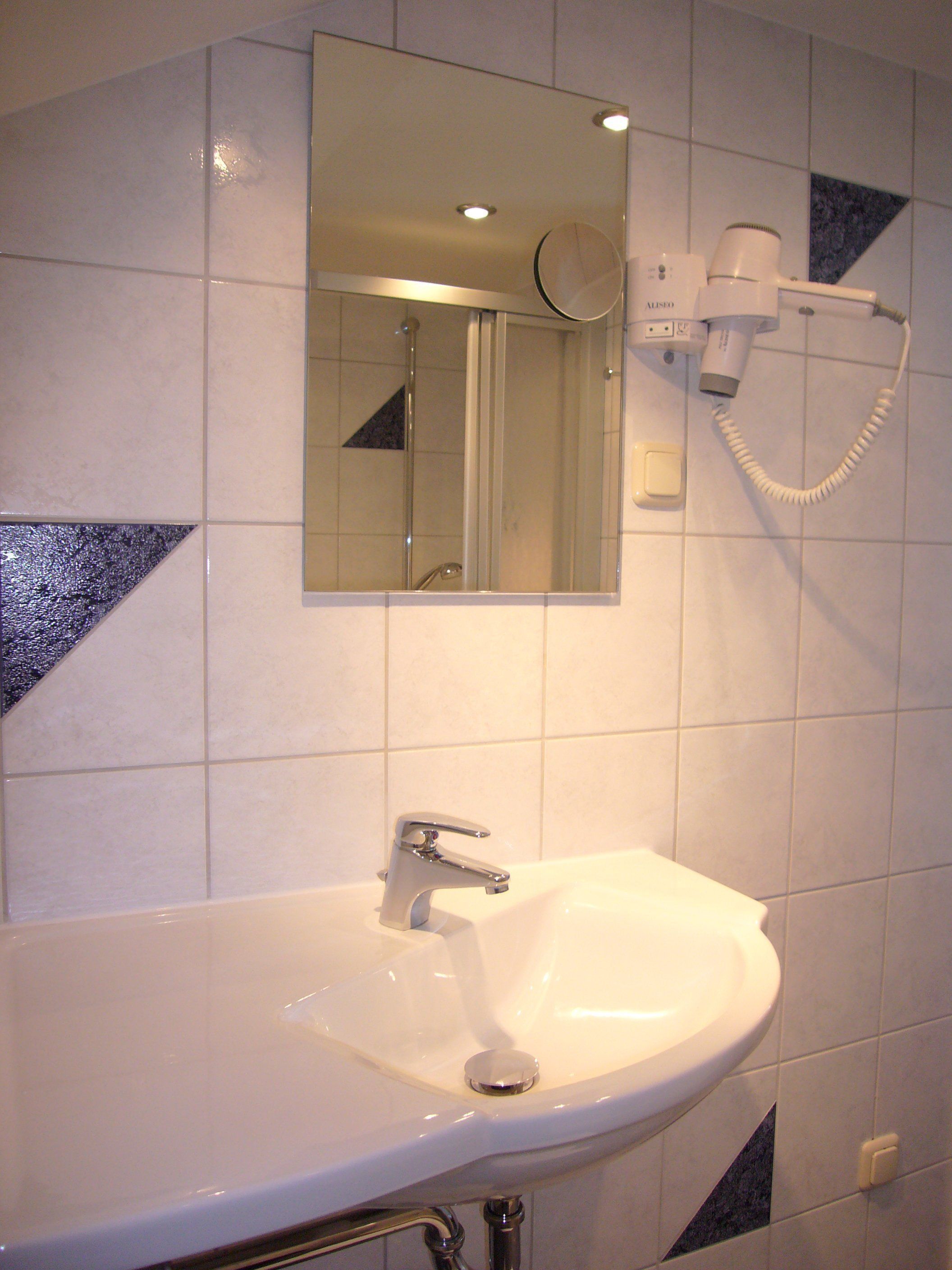 Un baño con un lavamanos blanco, un espejo y un secador de pelo montado en la pared.