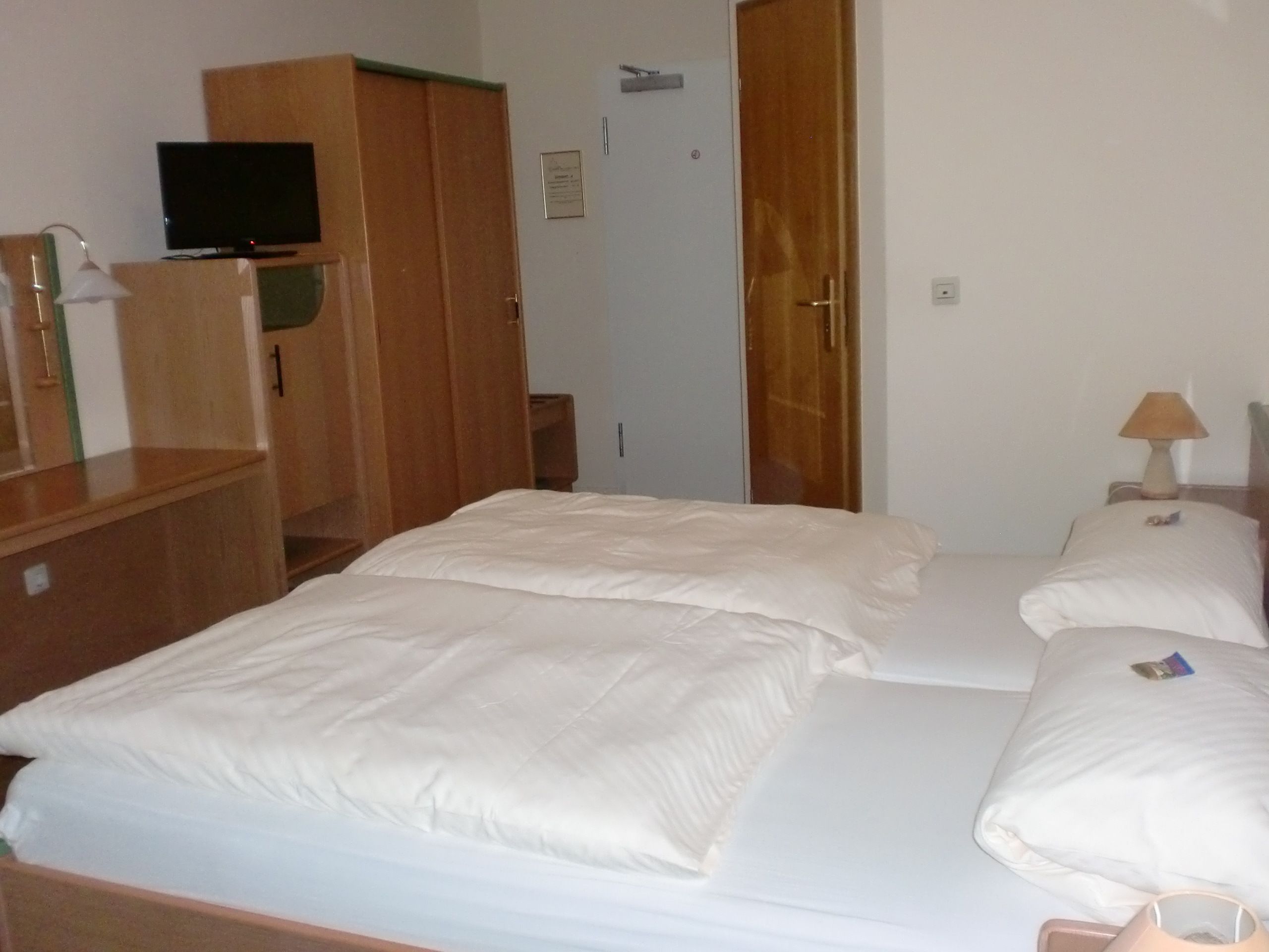 Une chambre d’hôtel avec un lit, un téléviseur posé sur une commode en bois et une porte.