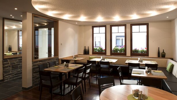 A restaurant with a stone wall, wooden tables, and a ceiling with a perforated design. - Hotel Deutsches Haus (Kaub)