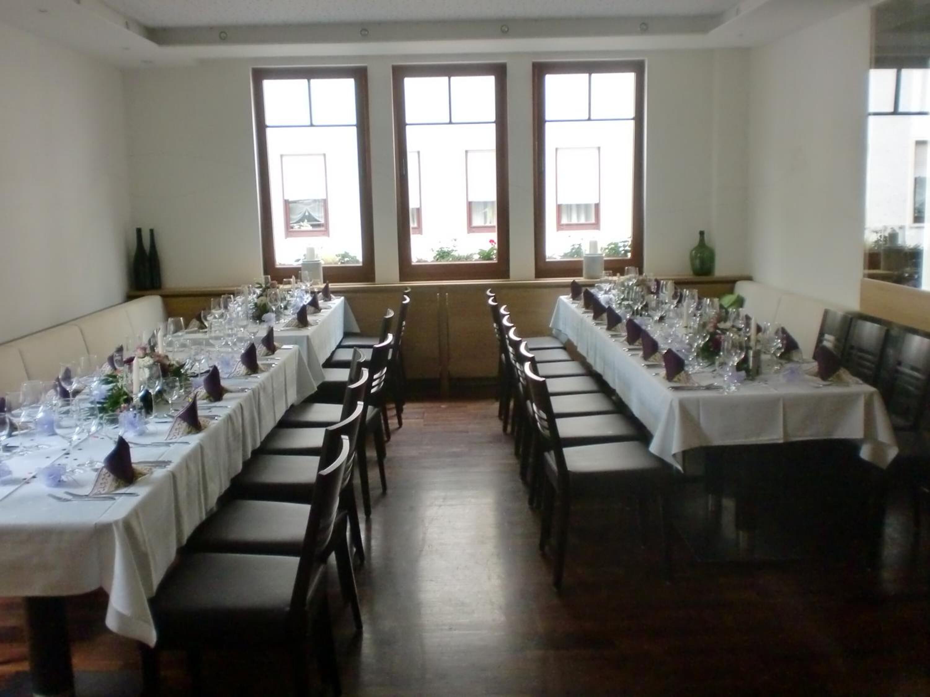 Un comedor con mesas largas dispuestas para una comida, ventanas amplias y vistas al exterior.