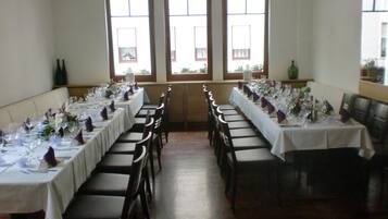 Un comedor con mesas largas dispuestas para una comida, ventanas amplias y vistas al exterior.