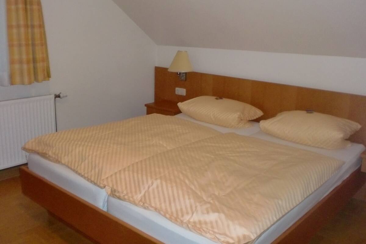 Een tweepersoonsbed met een gestreept dekbedovertrek, een houten hoofdbord en een bedlampje.