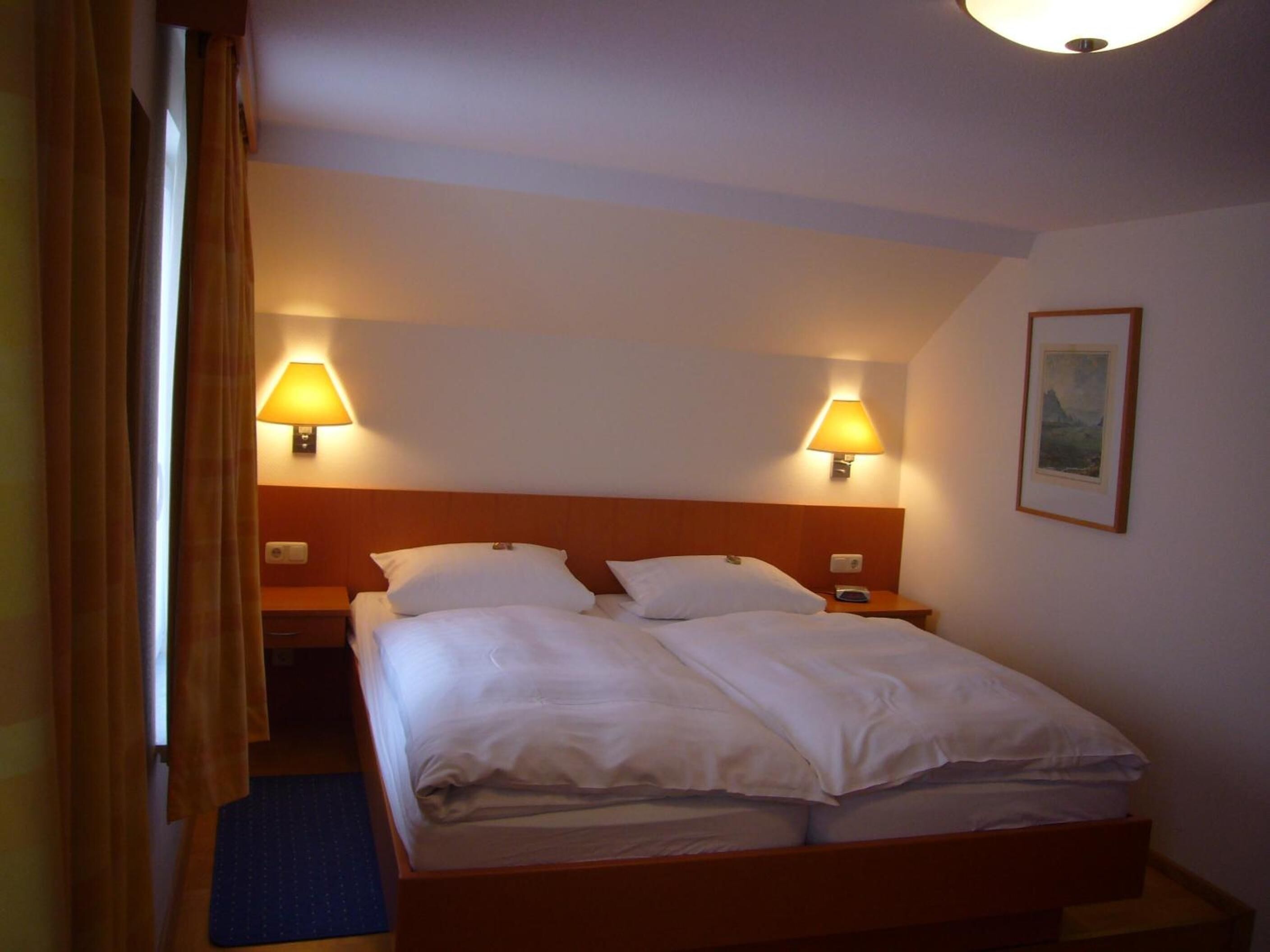 A double bed with two bedside tables, each with a lamp, in a hotel room.