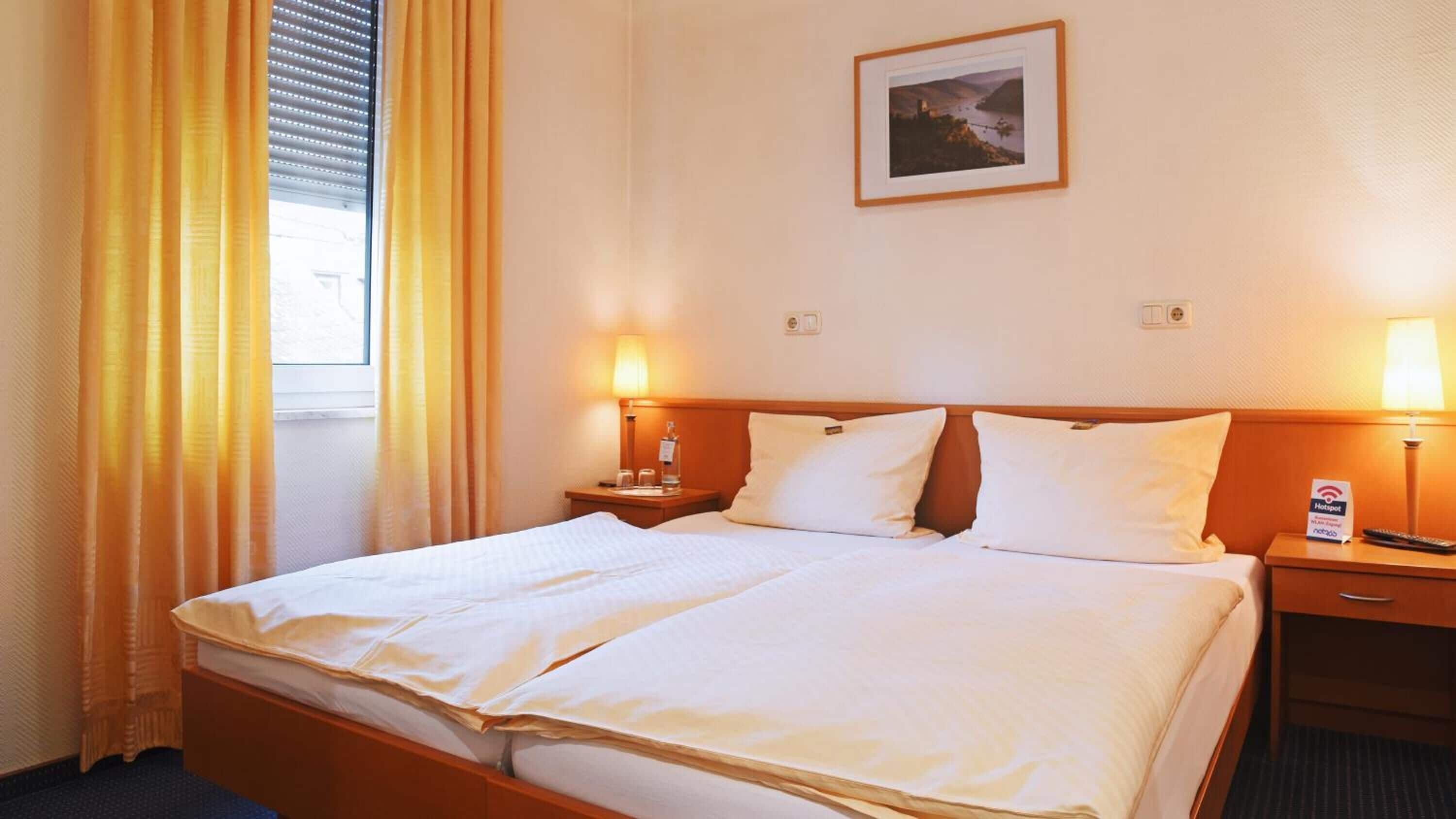 Une chambre d’hôtel avec un grand lit, deux tables de chevet avec des lampes, un tableau encadré au mur et une fenêtre avec des rideaux.