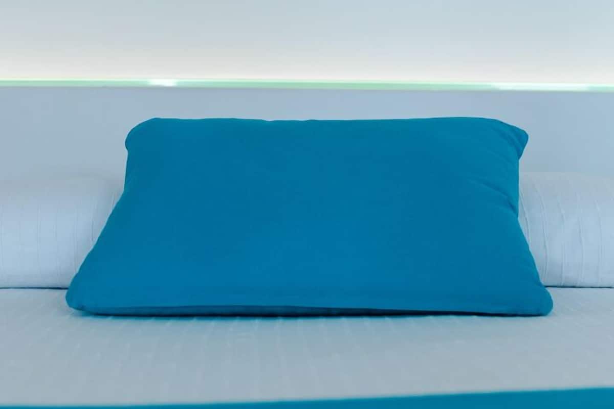 Un cojín azul verdoso sobre un sofá blanco frente a una pared blanca con una tira de luz verde.