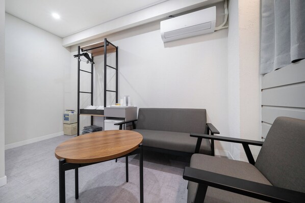 A modern, compact room with a sofa, a small table, a ladder, and an air conditioning unit.