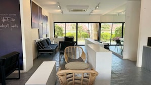 A modern coffee shop interior with wicker furniture, a bar area, and large windows offering a view of the outdoors. - Collection O The Singha Chiangmai Hotel (Chiang Mai)